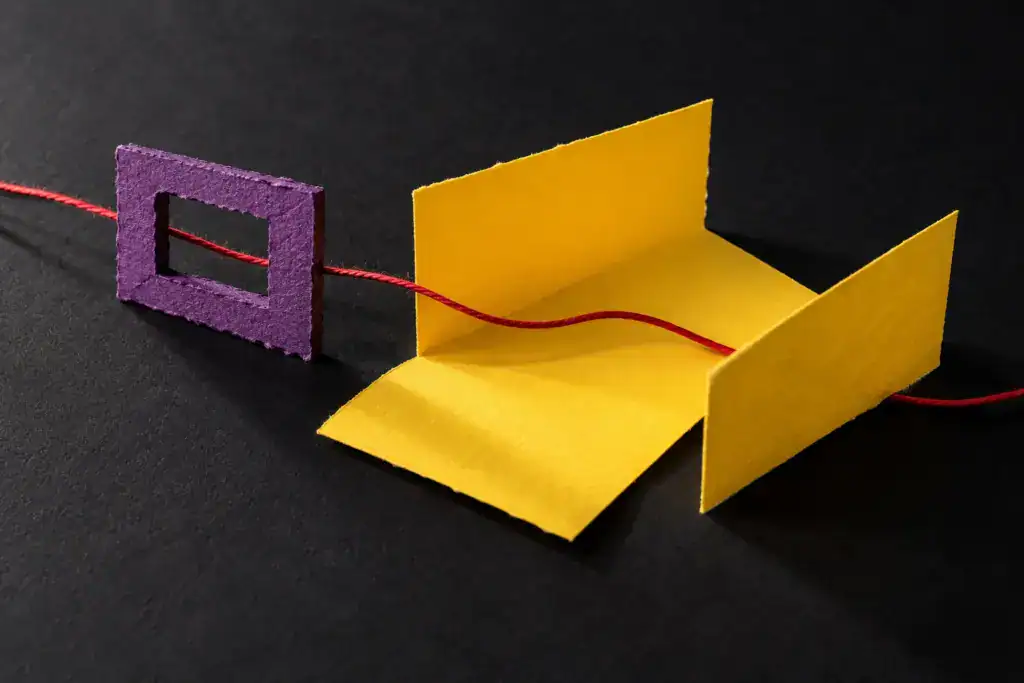 Ein roter Faden führt durch einen kleinen lila Rahmen in eine größere offene gelbe Papierform.